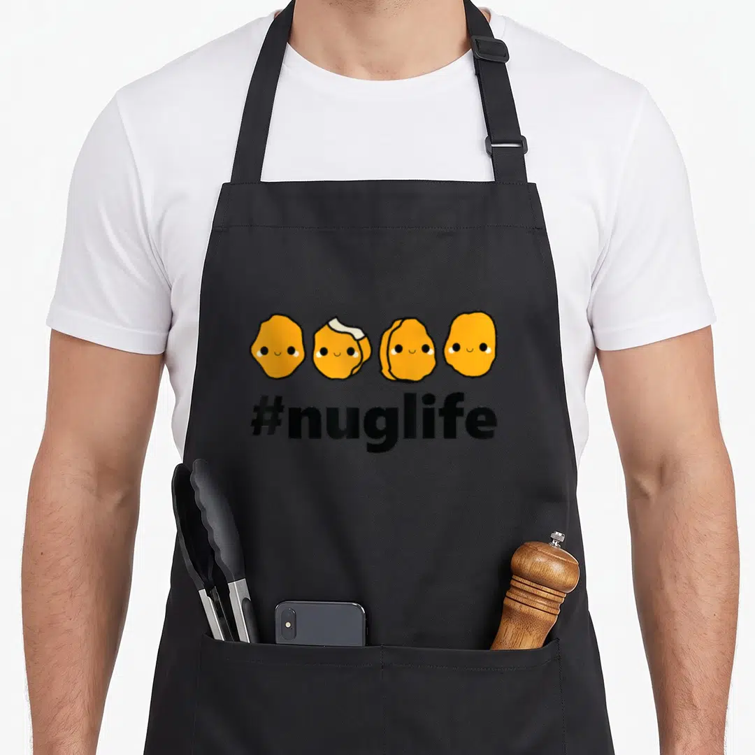 Funny nug chicken print apron - Four orange cartoon nuggets with smiley faces above black #nuglife text — shown on a black cotton canvas apron against a white background