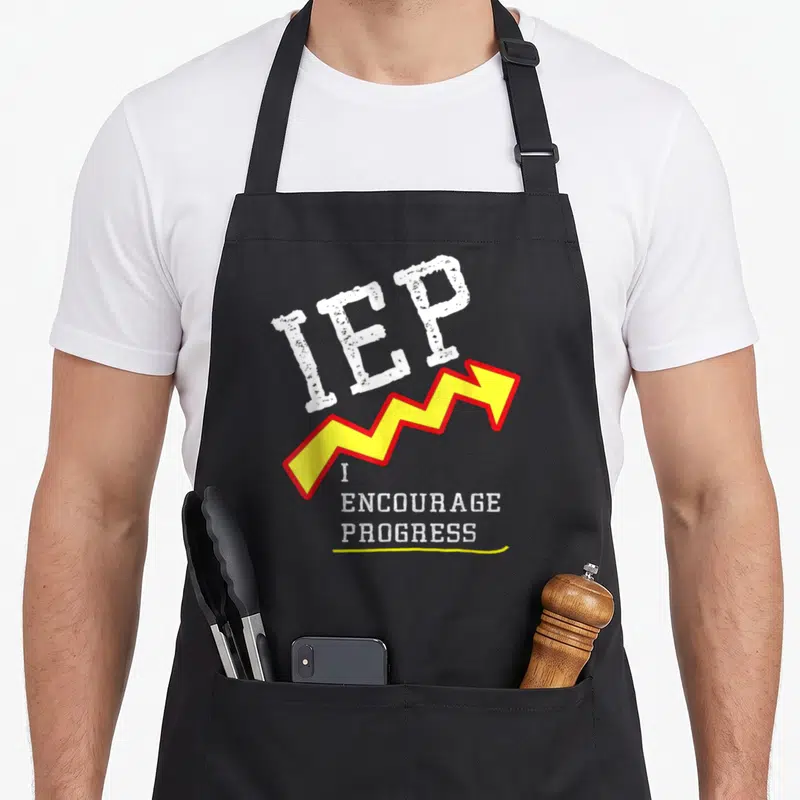 Mindful teacher apron - IEP text above jagged yellow arrow and I Encourage Progress slogan in distressed white font — shown on a black cotton canvas apron against a white background