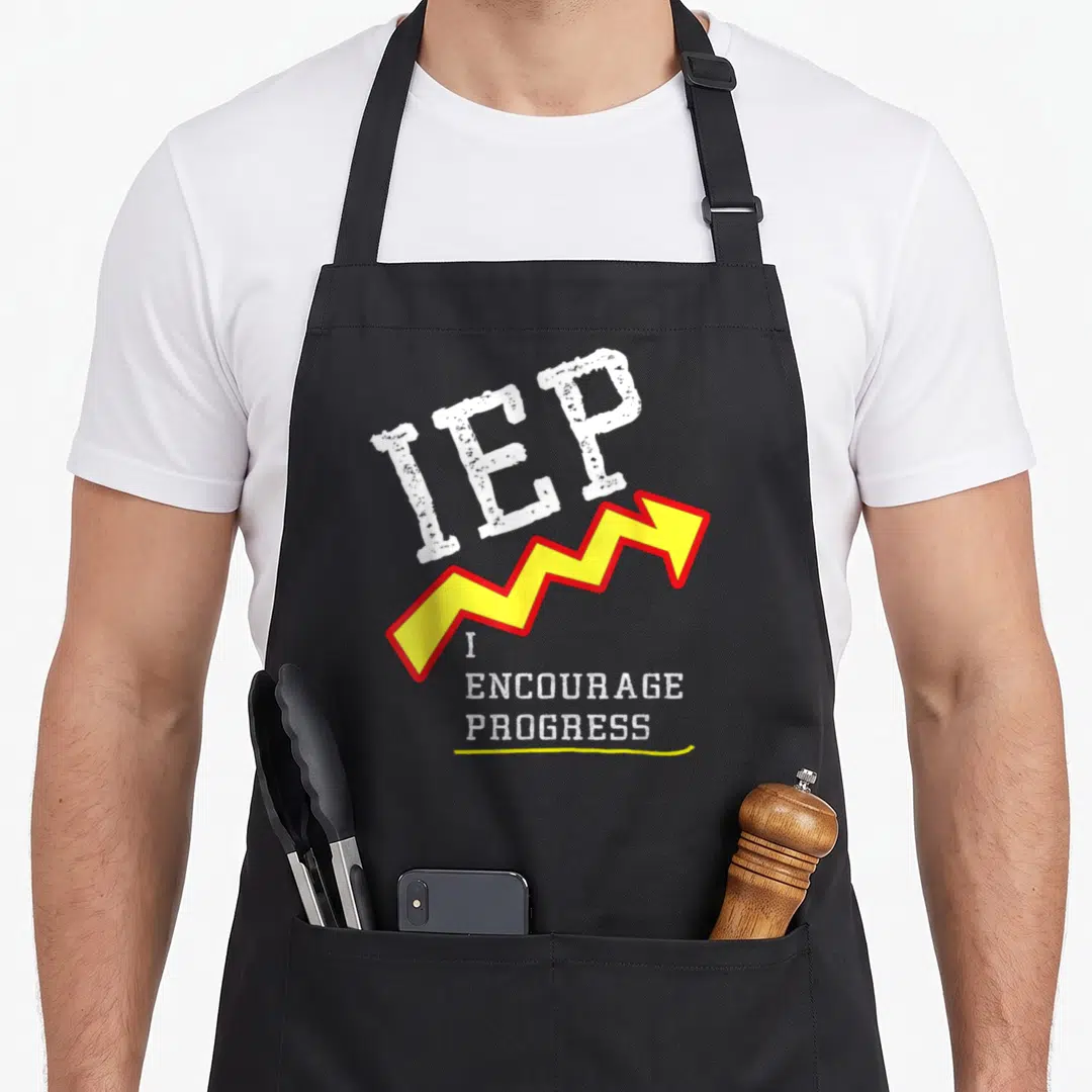 Mindful teacher apron - IEP text above jagged yellow arrow and I Encourage Progress slogan in distressed white font — shown on a black cotton canvas apron against a white background