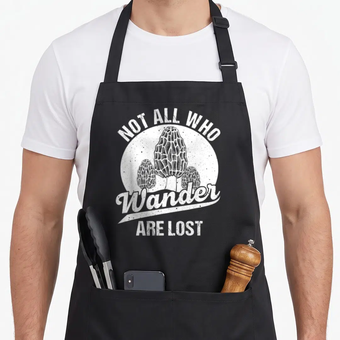 Hunter foraging apron - Three white morel mushrooms in a circle with text Not All Who Wander Are Lost — shown on a black cotton canvas apron against a white background