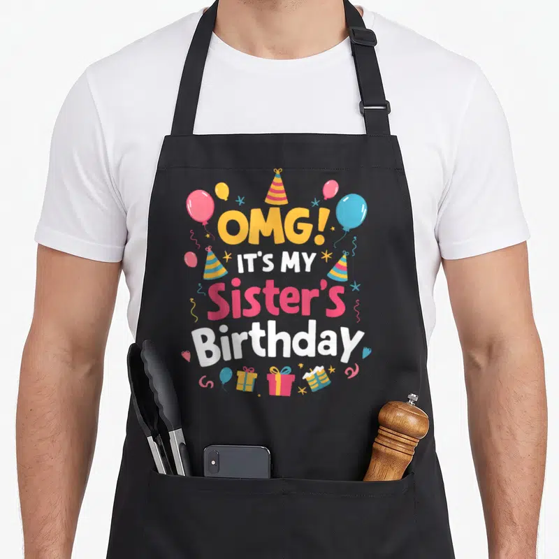 Squad omg birthday apron - Stacked text OMG Sister Birthday with cartoon balloons, striped hats, and gifts in yellow — shown on a black cotton canvas apron against a white background