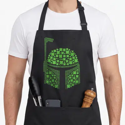 Clover irish girl apron - Green shamrock mosaic forming a Stormtrooper helmet silhouette — shown on a black cotton canvas apron against a white background