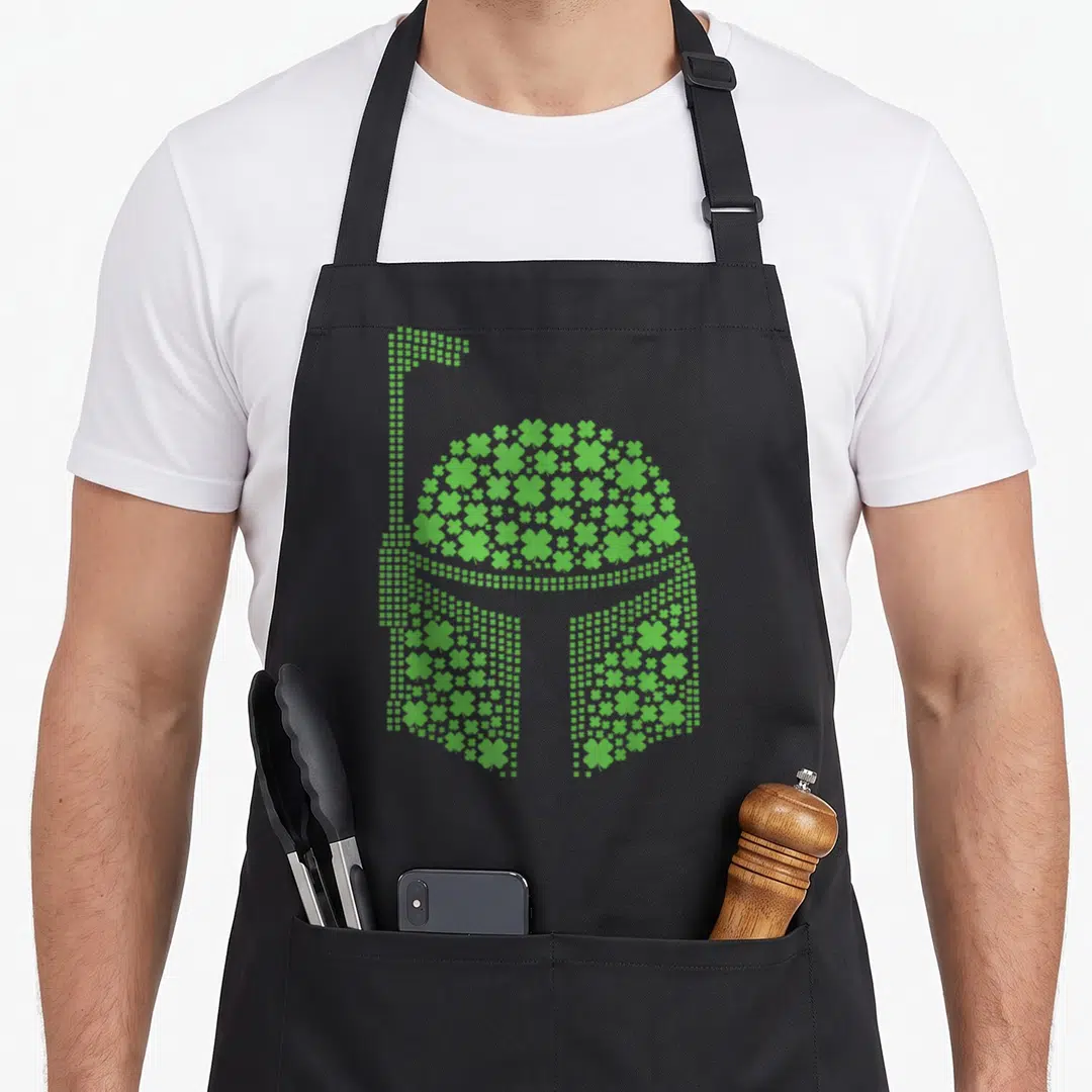 Clover irish girl apron - Green shamrock mosaic forming a Stormtrooper helmet silhouette — shown on a black cotton canvas apron against a white background