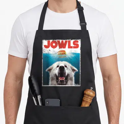 Gentle dog apron - Red Jowls text over burger floating in blue water with white dog head emerging below — shown on a black cotton canvas apron against a white background