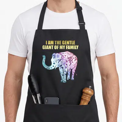 Elephant gentle apron - I AM THE GENTLE GIANT OF MY FAMILY text above a blue purple pink mandala elephant — shown on a black cotton canvas apron against a white background