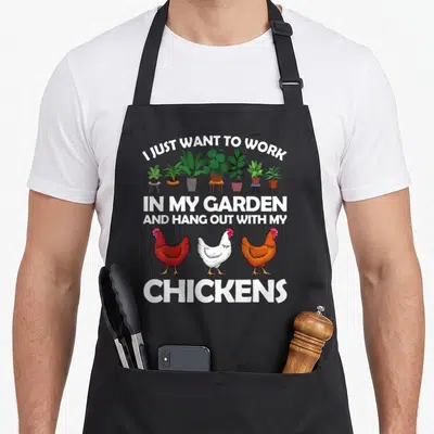 Gardening chicken apron - Three cartoon chickens and potted plants surrounding text about working in a garden — shown on a black cotton canvas apron against a white background
