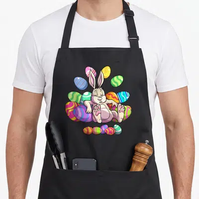 Funny easter bunny apron - Cartoon bunny sitting among purple pink yellow green and blue eggs — shown on a black cotton canvas apron against a white background