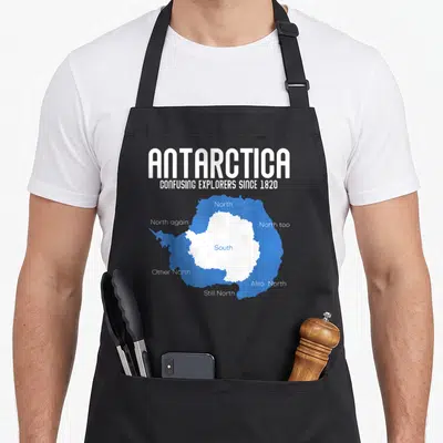 Antarctica explorer apron - White and blue map of Antarctica with South center and multiple North labels surrounding it — shown on a black cotton canvas apron against a white background