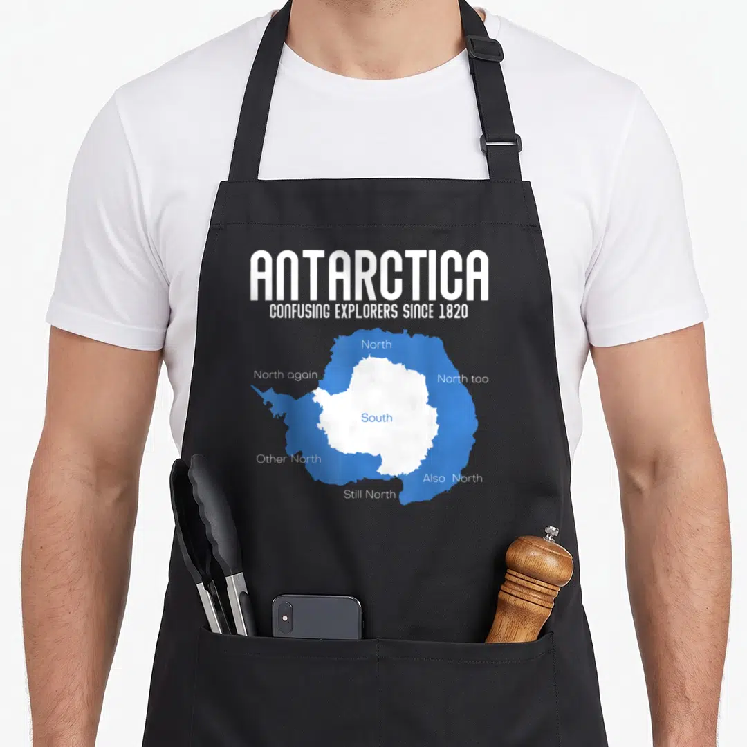 Antarctica explorer apron - White and blue map of Antarctica with South center and multiple North labels surrounding it — shown on a black cotton canvas apron against a white background