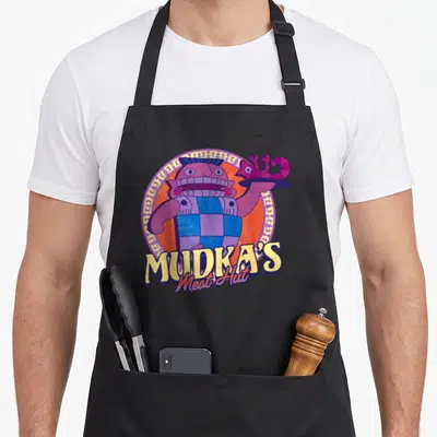 Emperor meat aprons - Purple cartoon character holding chameleon plate in orange circle with Mudka's Meat Hut text — shown on a black cotton canvas apron against a white background