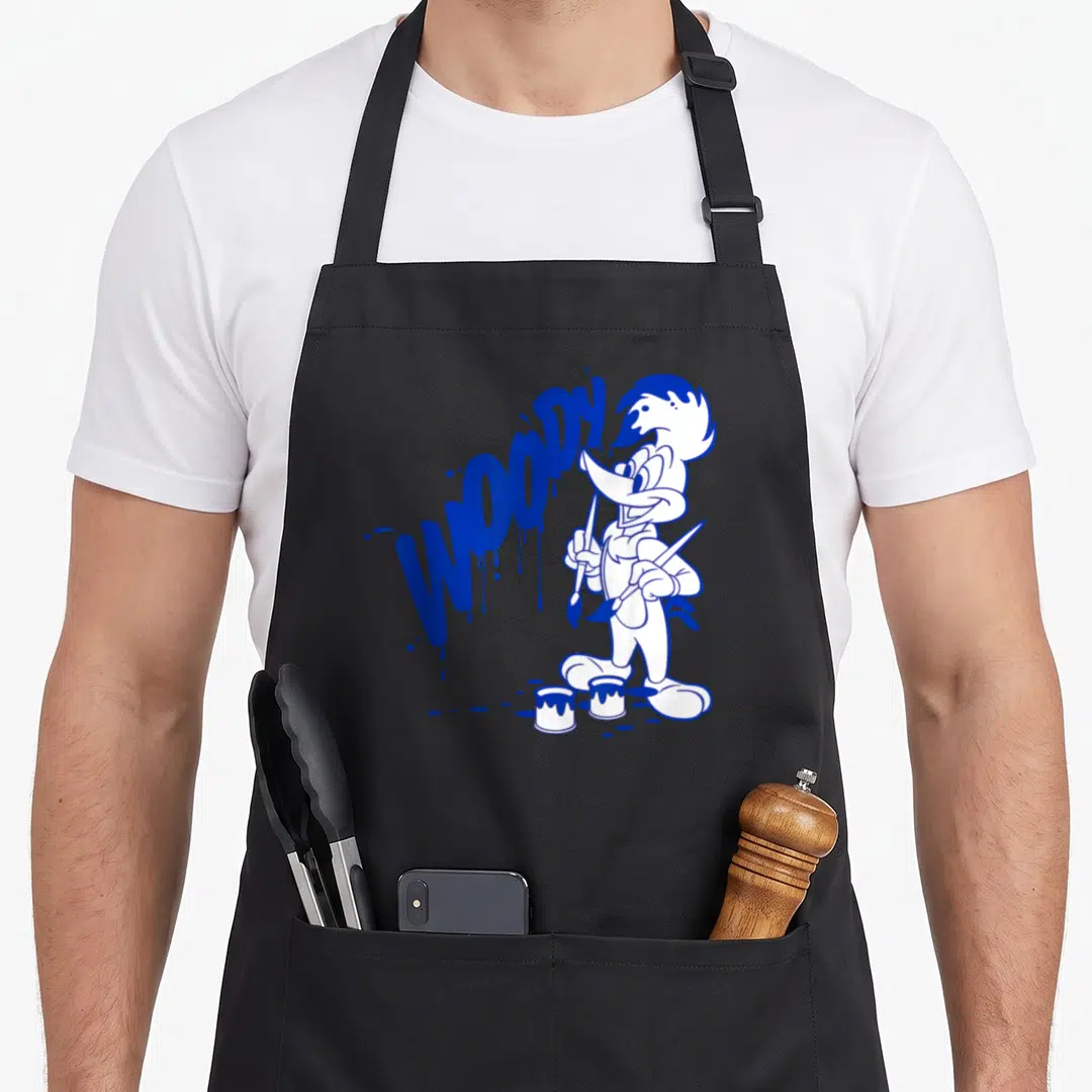 Blue paint apron - Cartoon woodpecker holding two brushes beside blue dripping text WOODY and two paint cans — shown on a black cotton canvas apron against a white background