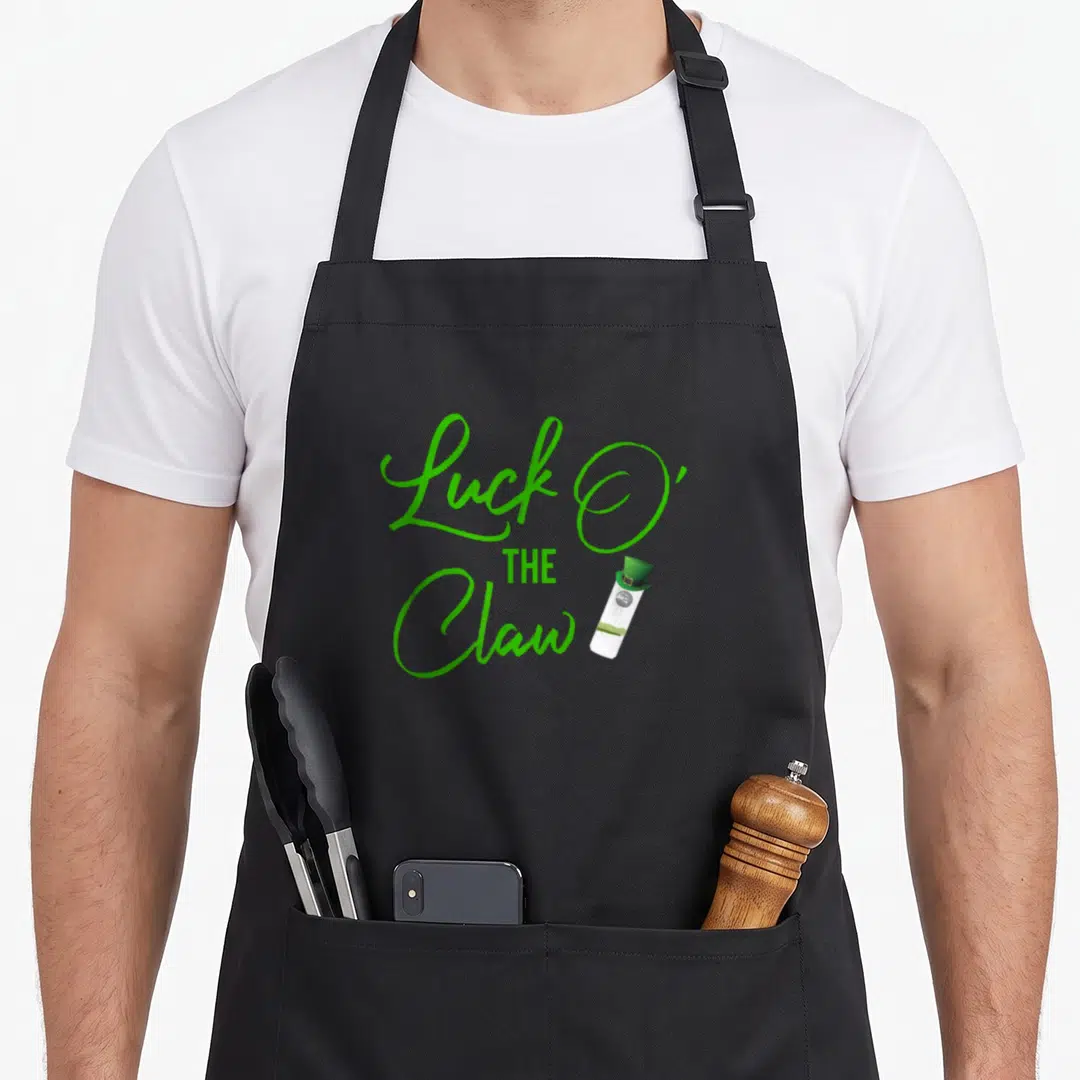 Luck seltzer apron - Green Luck O The Claw text with white prize wearing a hat — shown on a black cotton canvas apron against a white background