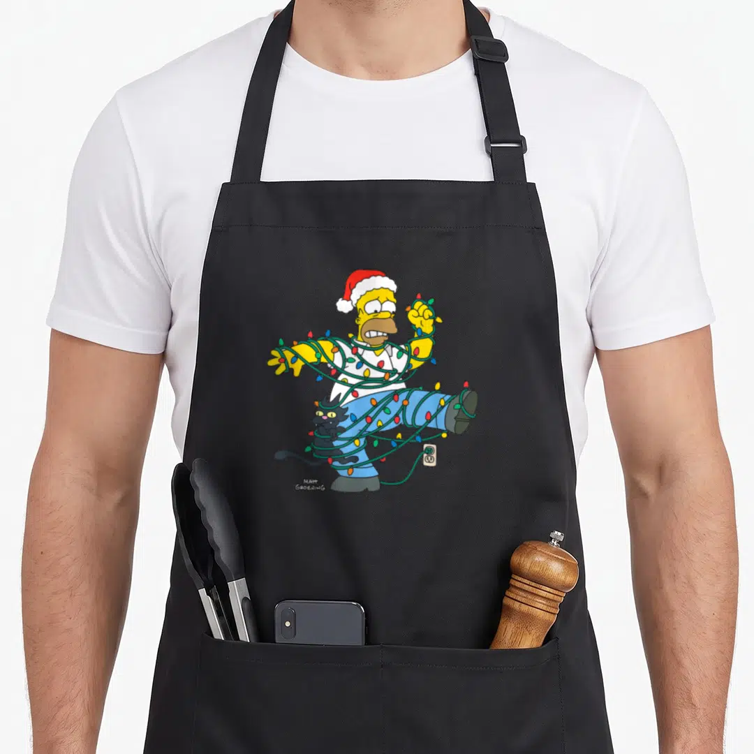 Homer christmas lights apron - Cartoon yellow character tangled in green Christmas lights with black cat and outlet plug — shown on a black cotton canvas apron against a white background