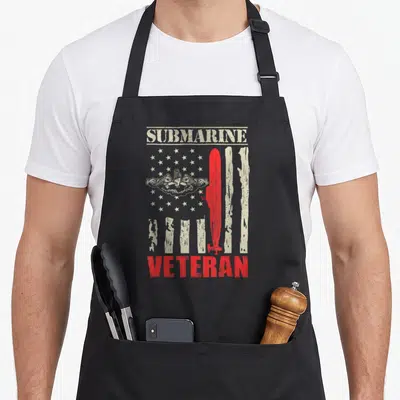 Cute submarine military apron - Red submarine over distressed beige stars and stripes with SUBMARINE VETERAN text — shown on a black cotton canvas apron against a white background