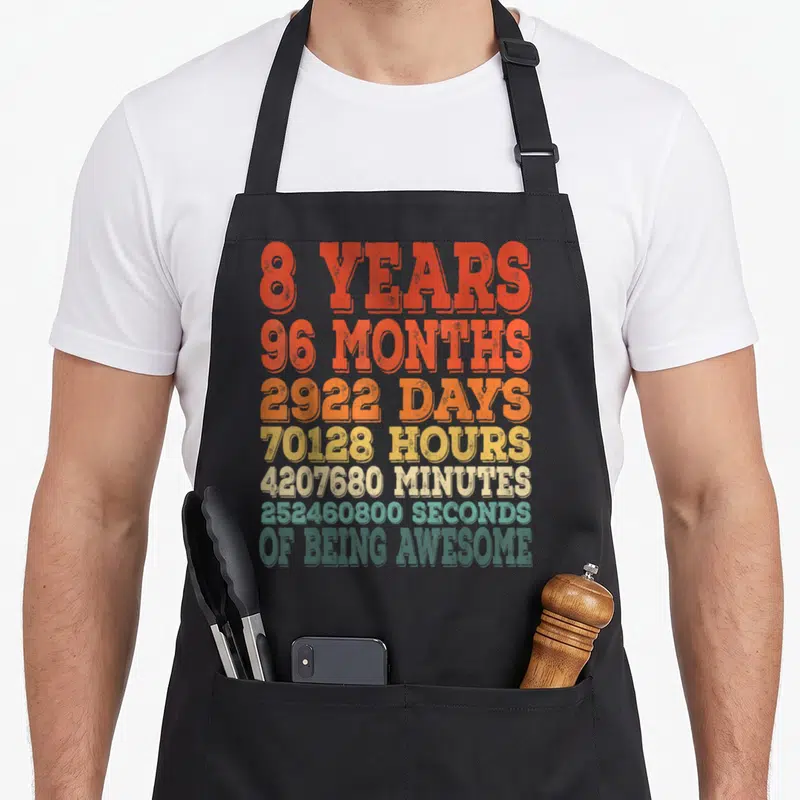 8th eighth birthday apron - Stacked distressed text listing 8 years and seconds of being awesome in rainbow colors — shown on a black cotton canvas apron against a white background