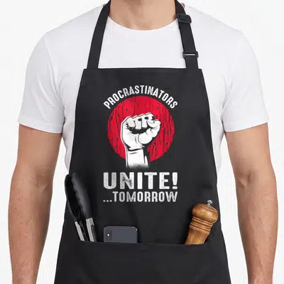Sarcasm procrastinator apron - White fist inside red circle with text Procrastinators Unite Tomorrow in distressed font — shown on a black cotton canvas apron against a white background