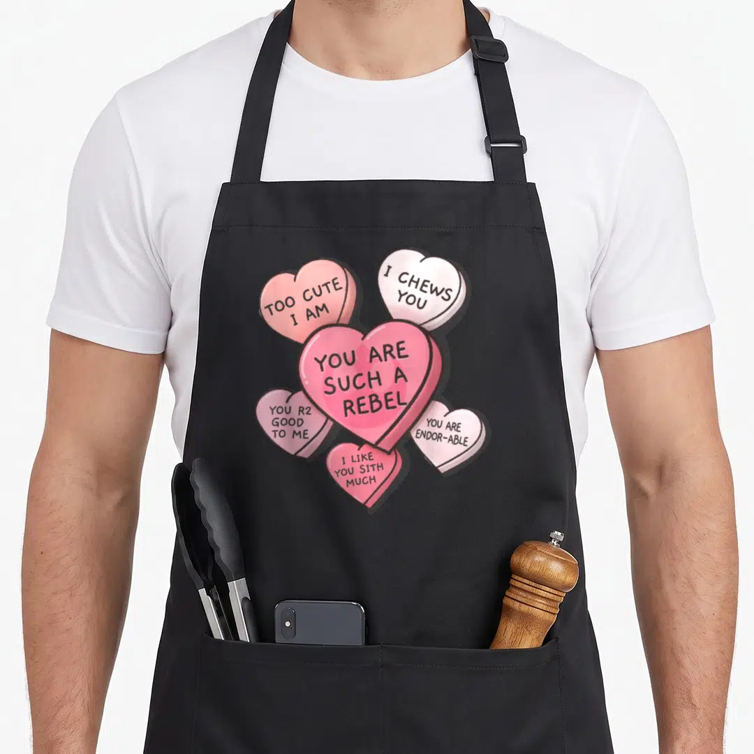 Funny valentine cotton candy apron - Five pink and white candy hearts with Star Wars pun text like You Are Such A Rebel — shown on a black cotton canvas apron against a white background