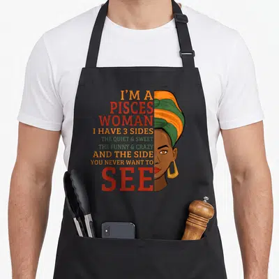 Funny pisces girl apron - Stacked text listing three sides next to a cartoon portrait of a woman wearing a striped — shown on a black cotton canvas apron against a white background