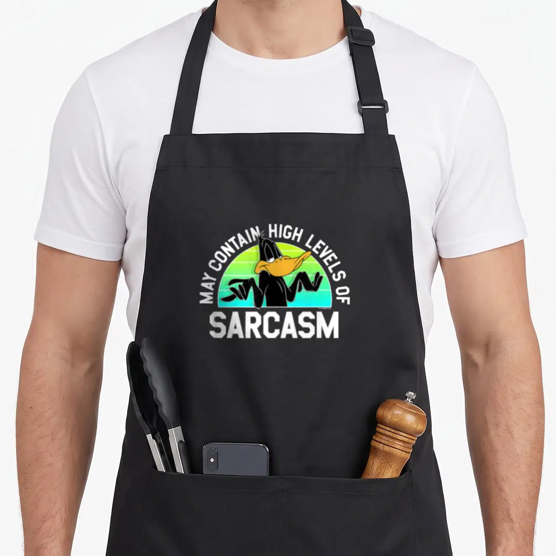 Contain duck apron - Cartoon duck shrugging in front of green sun with text MAY CONTAIN HIGH LEVELS OF SARCASM — shown on a black cotton canvas apron against a white background