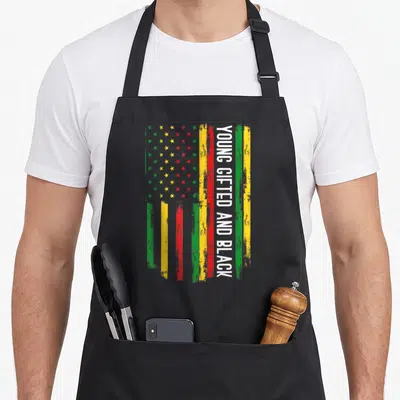 Young pride apron - Distressed flag with green yellow red stripes and vertical white text Young Gifted and Black — shown on a black cotton canvas apron against a white background