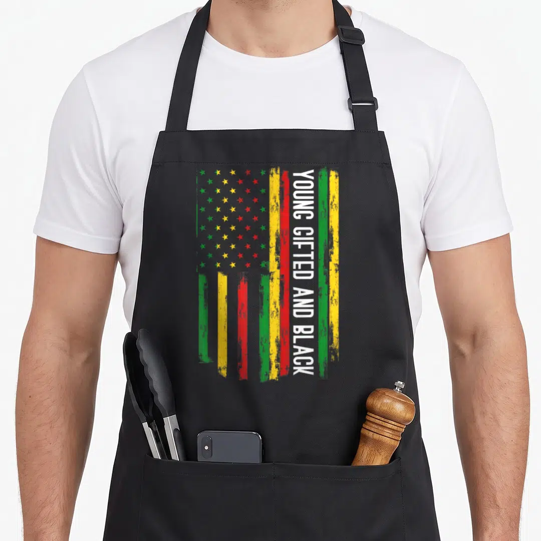 Young pride apron - Distressed flag with green yellow red stripes and vertical white text Young Gifted and Black — shown on a black cotton canvas apron against a white background