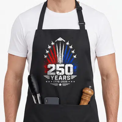 Jet patriotic apron - 250 YEARS 1776-2026 jet planes red white blue distressed smoke trails — shown on a black cotton canvas apron against a white background