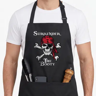 Surrender pirate apron - Distressed skull with red bandana and crossed bones under SURRENDER THE BOOTY text — shown on a black cotton canvas apron against a white background