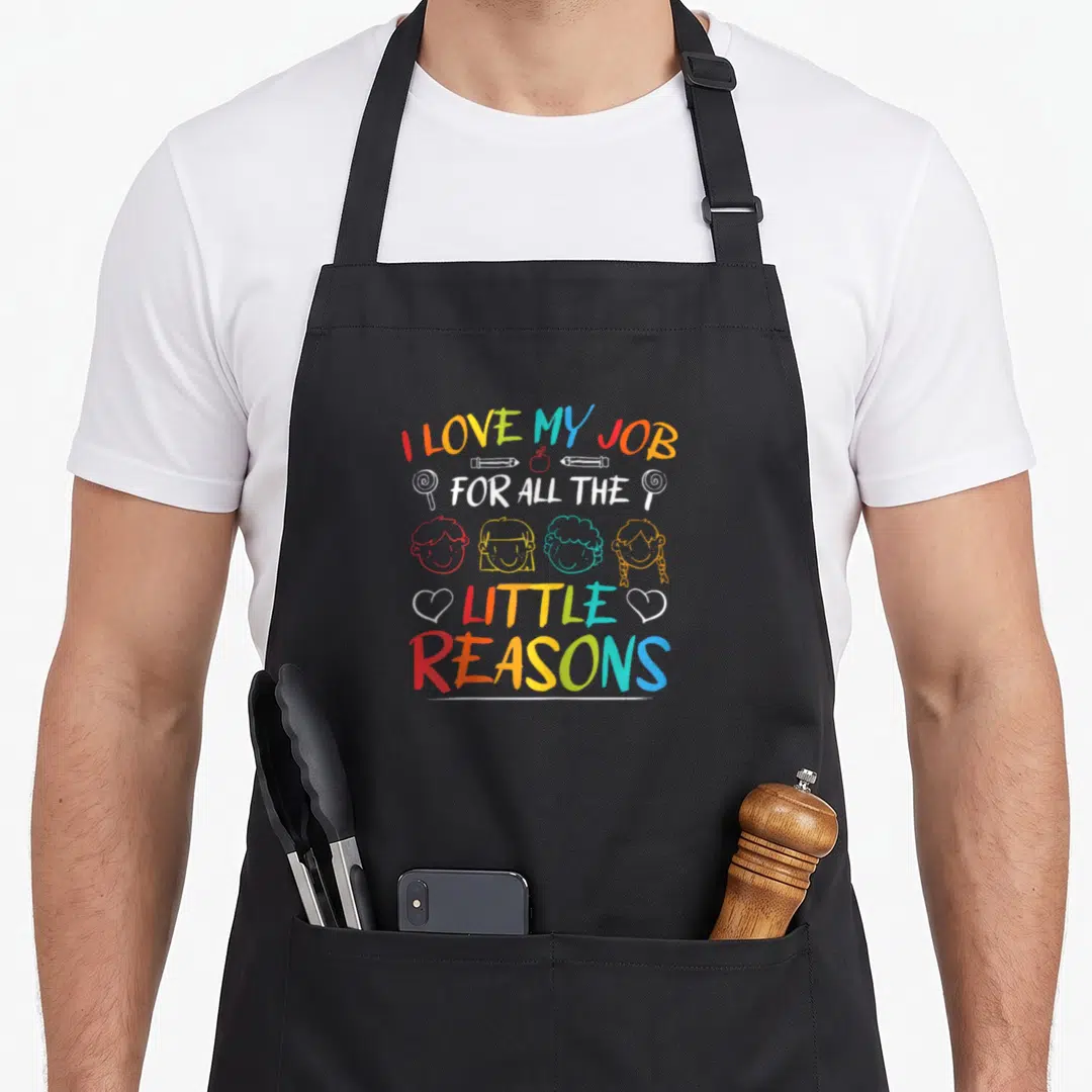 Passionate teacher apron - Stacked colorful text with row of four cartoon children heads and school supply doodles — shown on a black cotton canvas apron against a white background