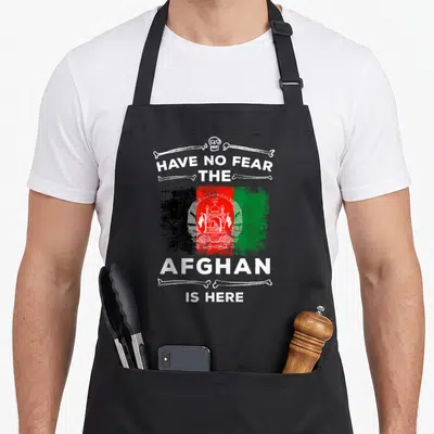 Afghanistan afghan apron - Distressed Afghan flag with HAVE NO FEAR THE AFGHAN IS HERE text and skull crossbones frame — shown on a black cotton canvas apron against a white background