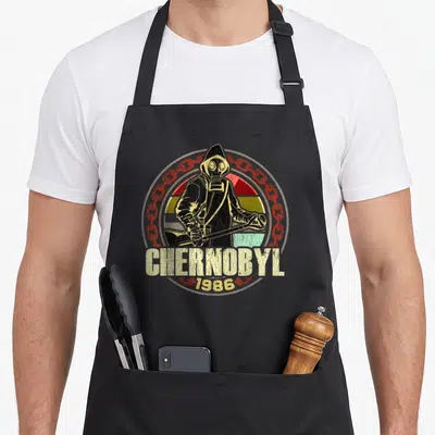 Chernobyl plant apron - Hazmat figure CHERNOBYL 1986 text red chain beige stripes distressed print — shown on a black cotton canvas apron against a white background
