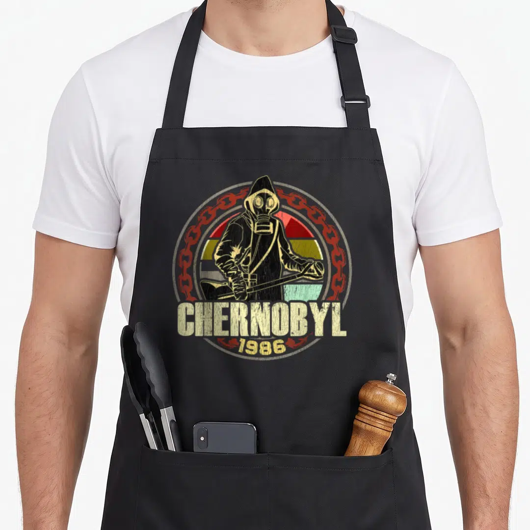 Chernobyl plant apron - Hazmat figure CHERNOBYL 1986 text red chain beige stripes distressed print — shown on a black cotton canvas apron against a white background