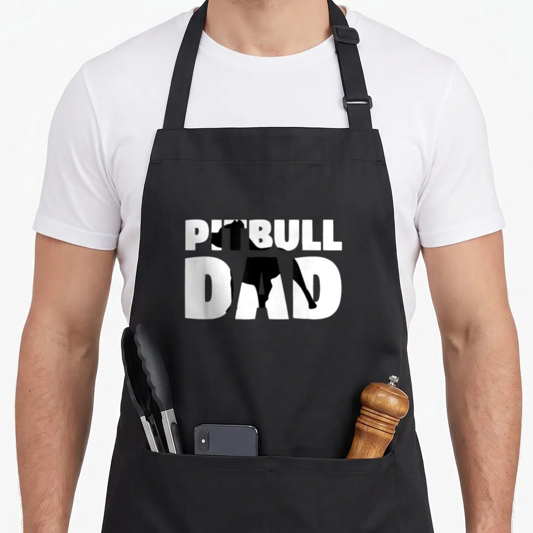 Pitbull pittie dog apron - Black pitbull silhouette integrated into stacked white PITBULL DAD text — shown on a black cotton canvas apron against a white background