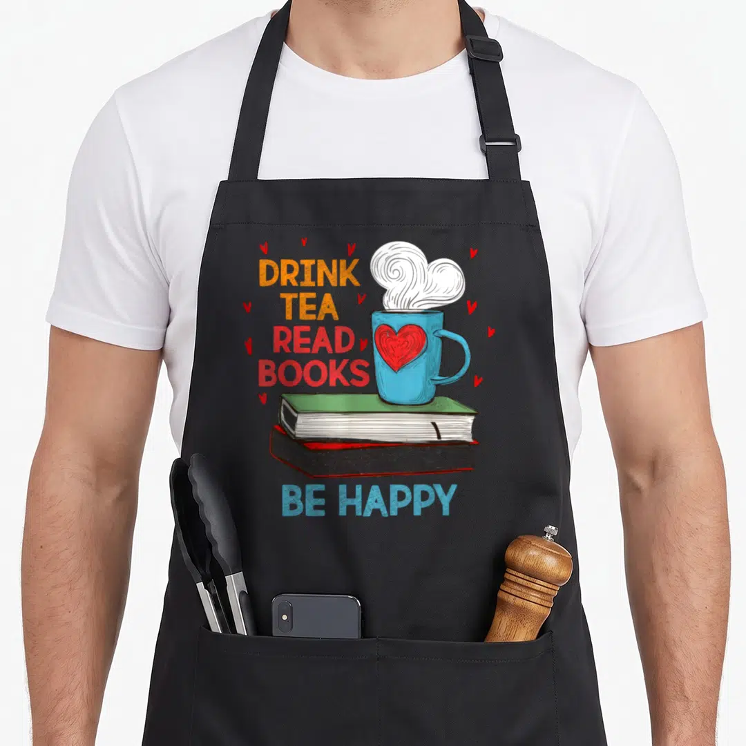 Book tea apron - Blue mug with red heart on stacked books surrounded by hearts and text — shown on a black cotton canvas apron against a white background