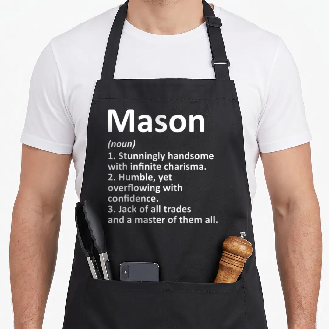 Definition mason apron - White text on grey background defining Mason as handsome, humble, and a master of trades — shown on a black cotton canvas apron against a white background