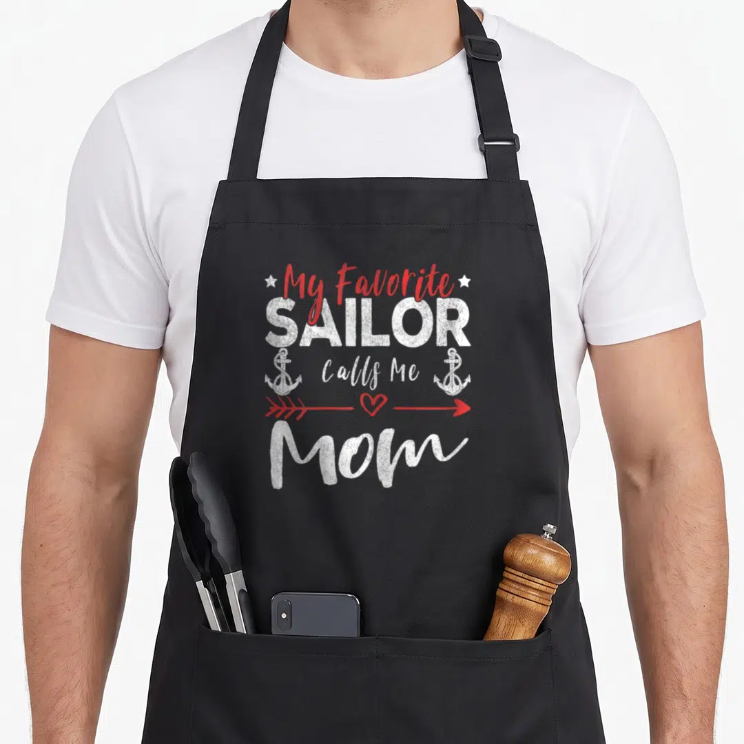 Sailor call mom apron - Distressed white and red text My Favorite Sailor Calls Me Mom with anchors and heart arrow — shown on a black cotton canvas apron against a white background