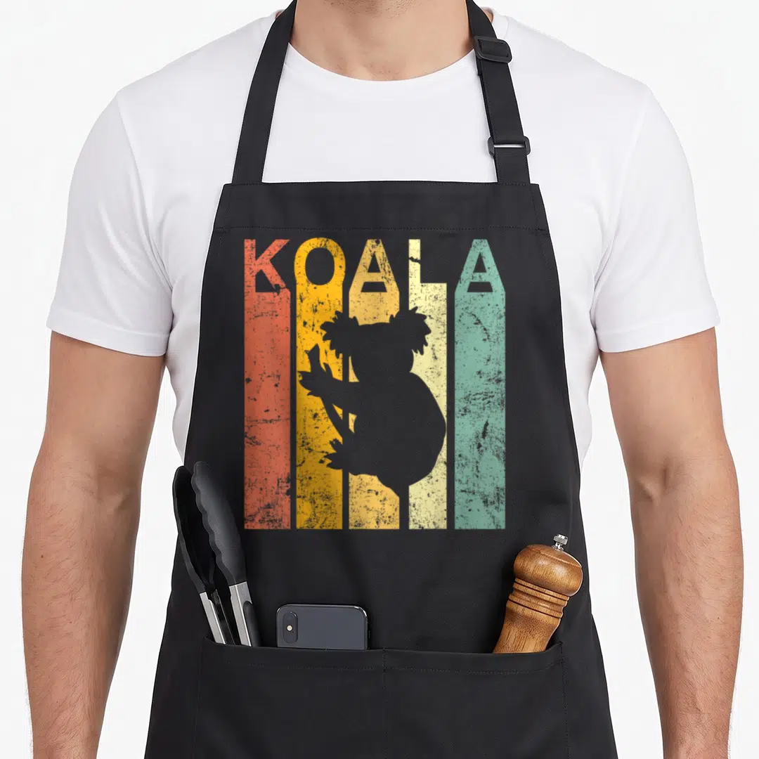 Funny koala bear apron - KOALA text in orange yellow cream teal grey stripes with grey koala silhouette on branch — shown on a black cotton canvas apron against a white background