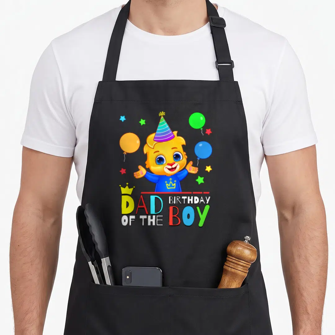 Celebrate lucas birthday apron - Cartoon lion cub with party hat and balloons above Dad of the Birthday Boy text — shown on a black cotton canvas apron against a white background