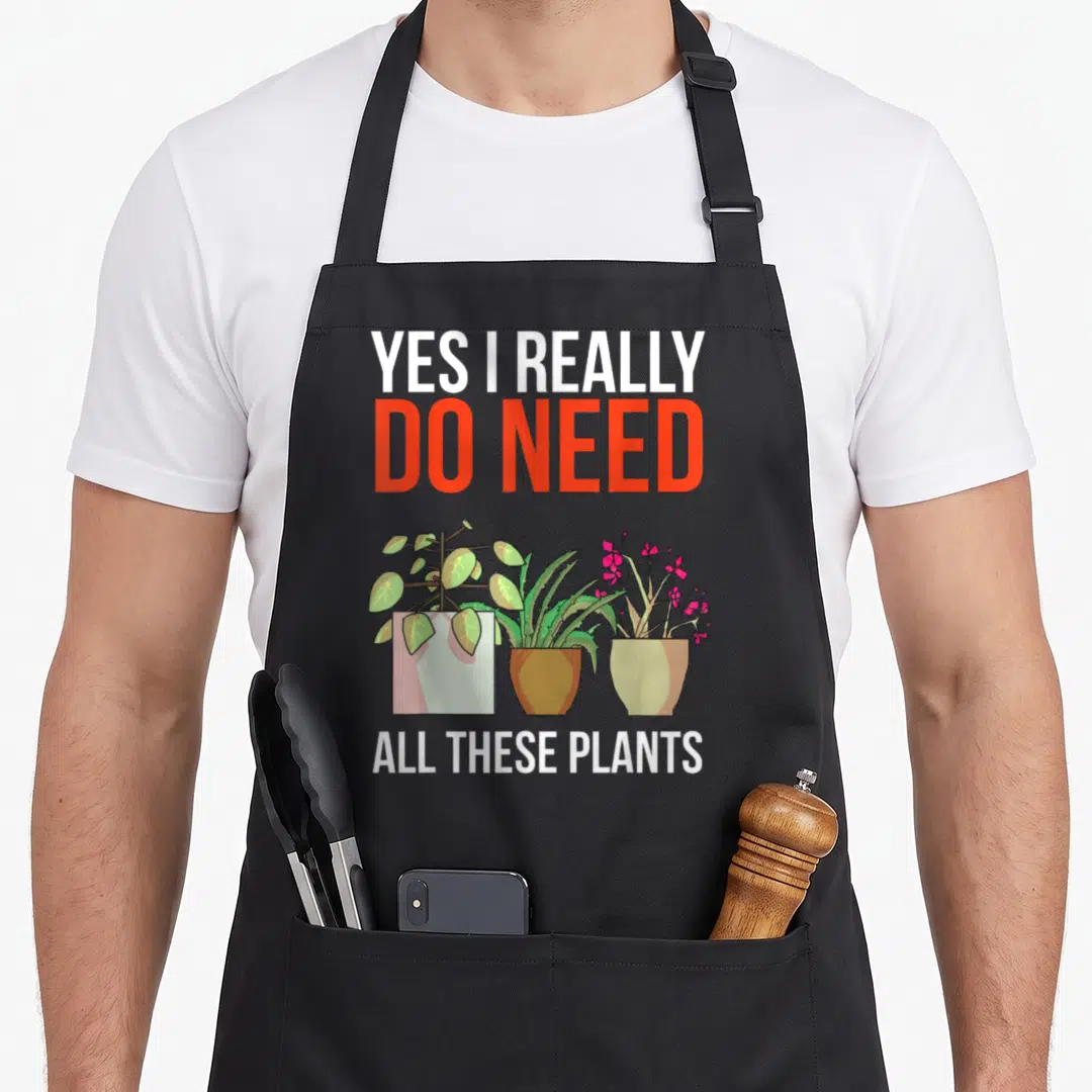 These plant do i need an apron - Yes I Really Do Need All These Plants text above three potted plants in cartoon style — shown on a black cotton canvas apron against a white background