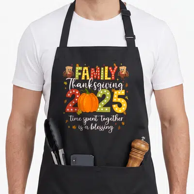 Crew turkey thanksgiving aprons - Cartoon turkeys flank FAMILY text above a pumpkin replacing the zero in 2025 script — shown on a black cotton canvas apron against a white background