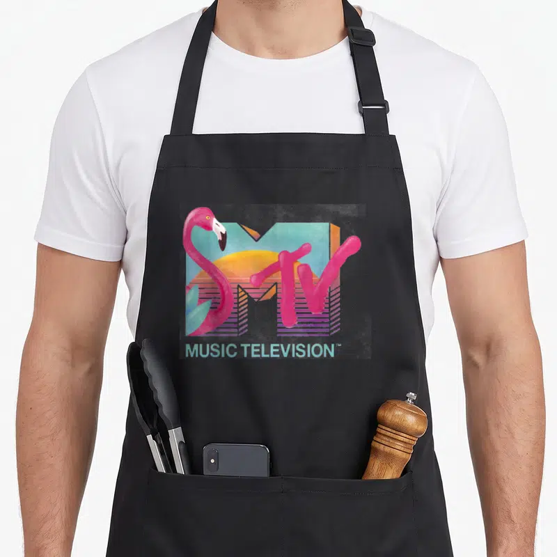 Distressed flamingo apron - Retro MTV logo with pink flamingo, sun, and MUSIC TELEVISION text in pastel colors — shown on a black cotton canvas apron against a white background