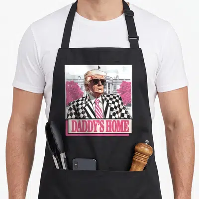 Donald daddy apron - Cartoon man in checkered suit with pink trees and DADDY'S HOME text banner — shown on a black cotton canvas apron against a white background