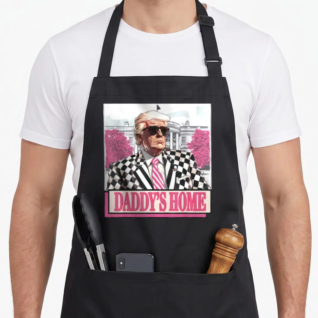 Donald daddy apron - Cartoon man in checkered suit with pink trees and DADDY'S HOME text banner — shown on a black cotton canvas apron against a white background