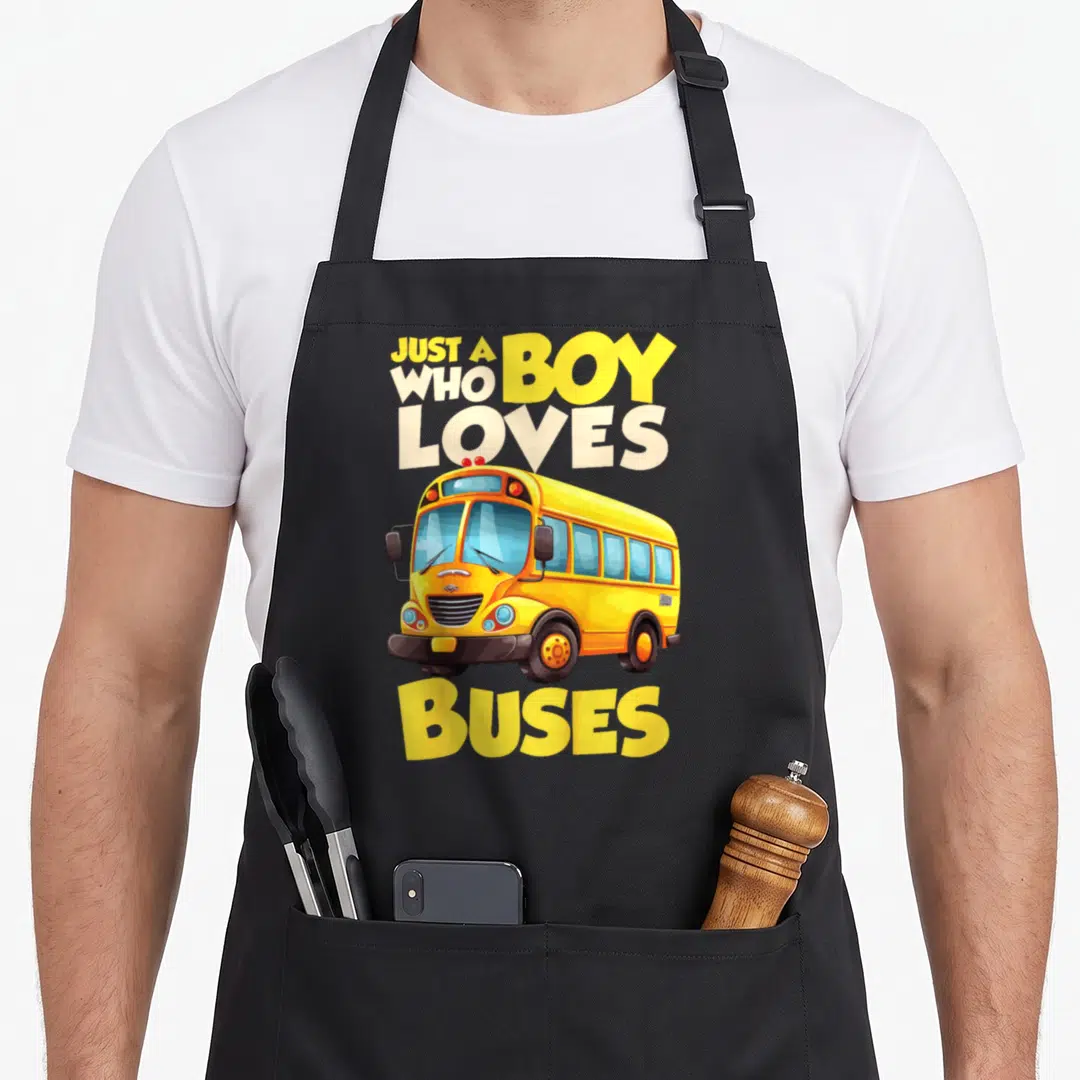 Funny buse school bus apron - Cartoon yellow school bus with text JUST A BOY WHO LOVES BUSES in white and blue lettering — shown on a black cotton canvas apron against a white background
