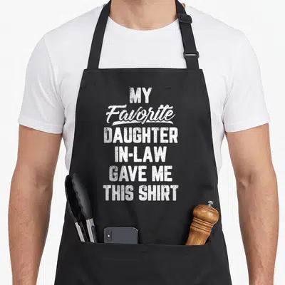 Law gave father day apron - White stacked typography reading My Favorite Daughter In Law Gave Me This Shirt on black — shown on a black cotton canvas apron against a white background