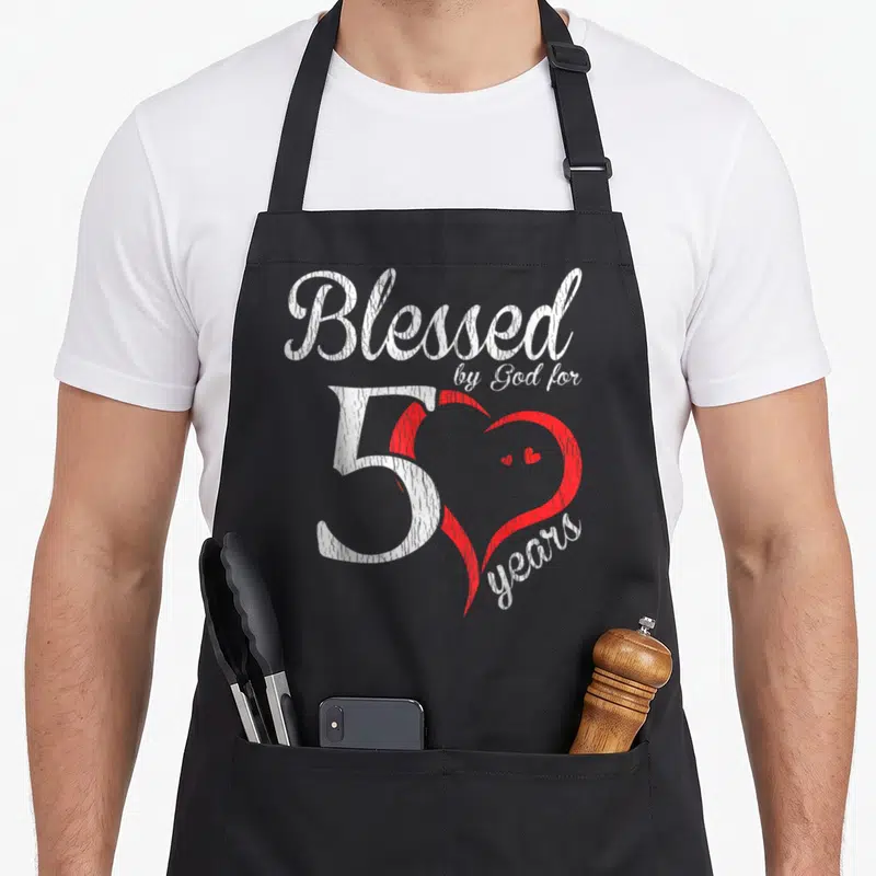 50th christian apron - White Blessed by God for 50 years text overlapping a red heart with years curved along bottom — shown on a black cotton canvas apron against a white background