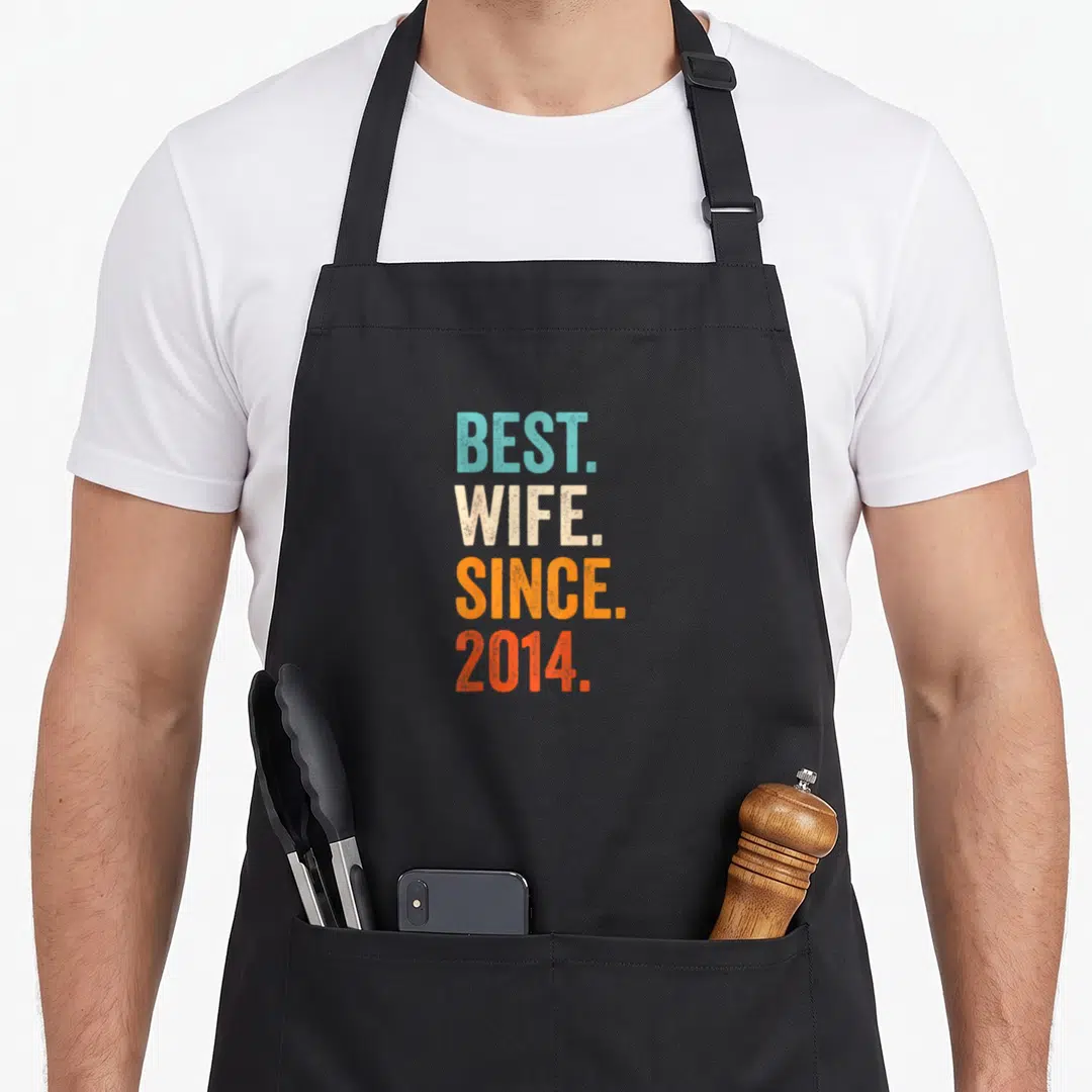 Wife wedding apron - Stacked BEST WIFE SINCE 2014 text in blue beige orange and red distressed letters — shown on a black cotton canvas apron against a white background