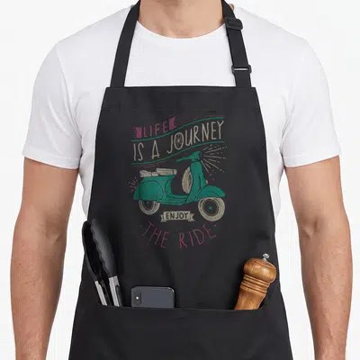 Journey biker life apron - Teal retro scooter with LIFE IS A JOURNEY ENJOY THE RIDE text in gold and pink — shown on a black cotton canvas apron against a white background