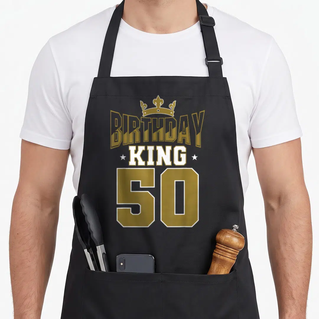 Theme kings apron - Gold and white BIRTHDAY KING 50 text with crown and stars on black bib — shown on a black cotton canvas apron against a white background