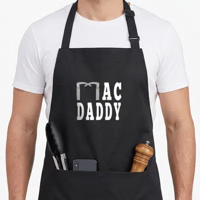 Anesthesia mac apron - MAC DADDY text with laryngoscope forming the letter M in white silver and green — shown on a black cotton canvas apron against a white background