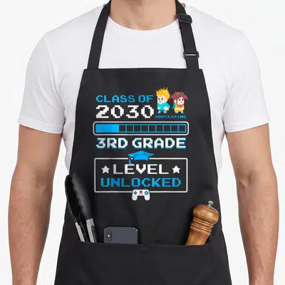 3rd grade video game apron - Pixel art text Class of 2030 Processing 3rd Grade Level Unlocked with characters — shown on a black cotton canvas apron against a white background